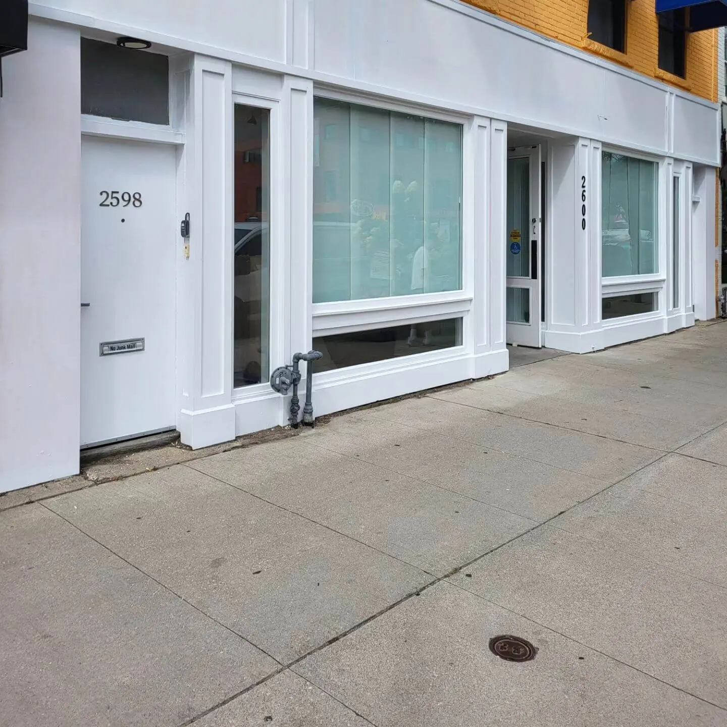 A street-level view of a clean white storefront with large glass windows and doors. A street-level view of a clean white storefront with large glass windows and doors.