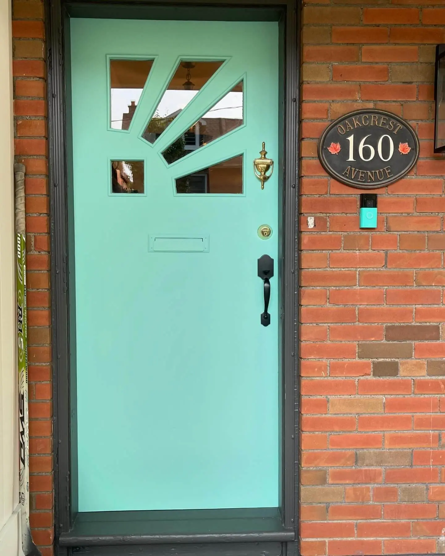 Close-up of a turquoise front door with unique window patterns, house number plaque reading '160 Oakcrest Avenue,' and a modern black door handle.