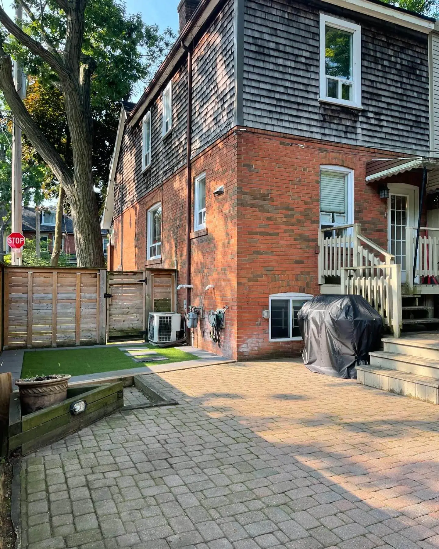 Backyard of a brick house featuring a paved patio, small artificial turf area, wooden fence, and outdoor air conditioning unit. Backyard of a brick house featuring a paved patio, small artificial turf area, wooden fence, and outdoor air conditioning unit.