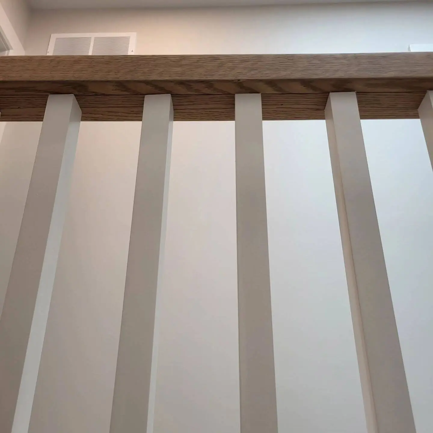 Close-up of white vertical balusters and a wooden handrail, emphasizing the minimalistic staircase design.