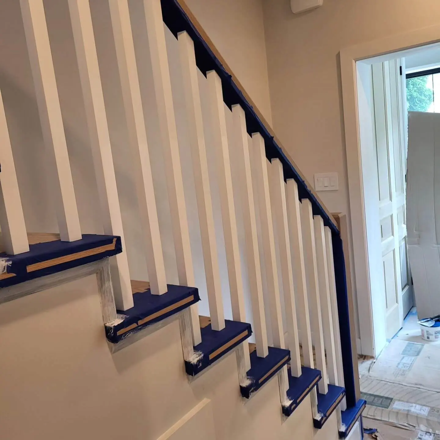 Staircase with white balusters and wooden treads, prepped with blue painter's tape for painting.