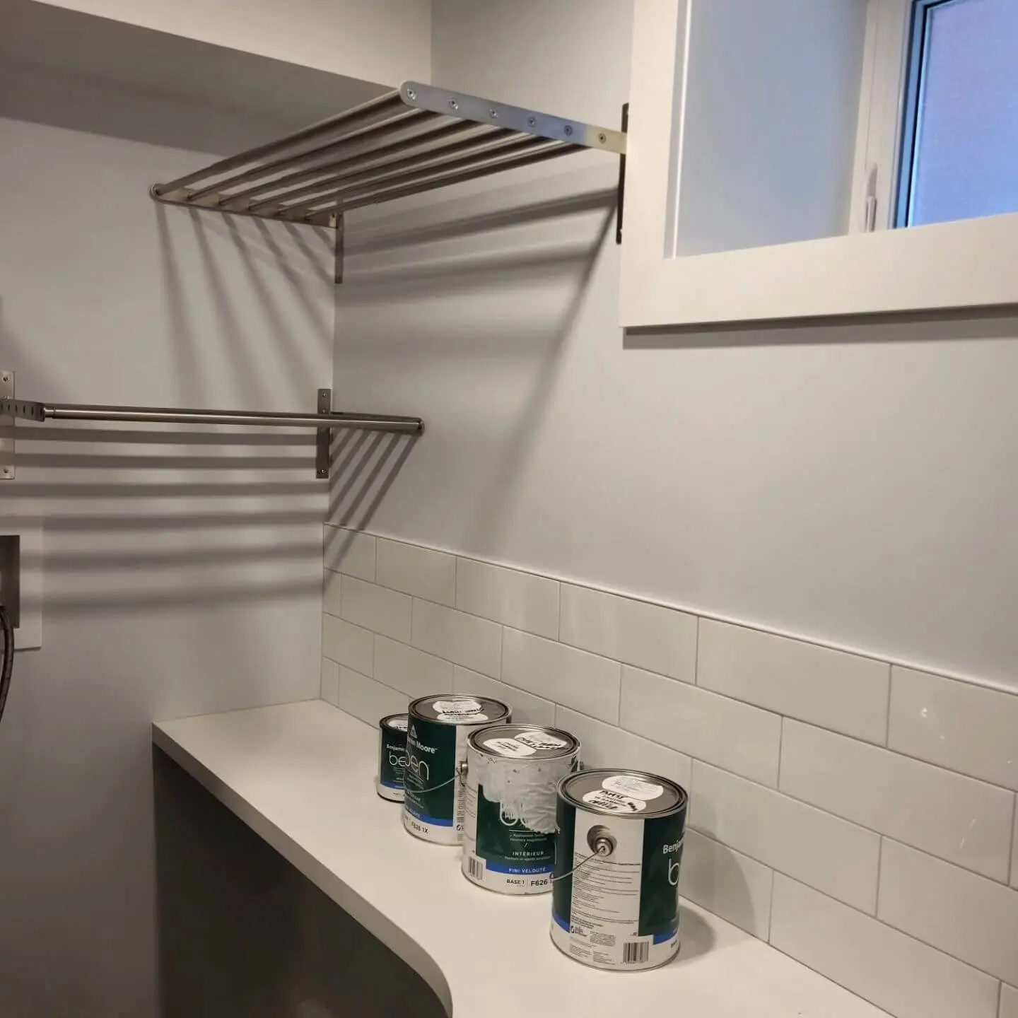Laundry room with a drying rack, tiled backsplash, and paint cans on a white countertop.