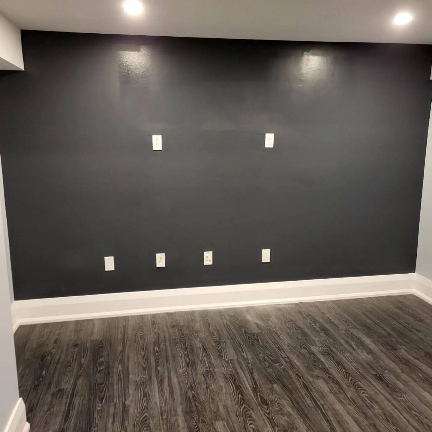Dark gray painted wall with electrical outlets and bright lighting.