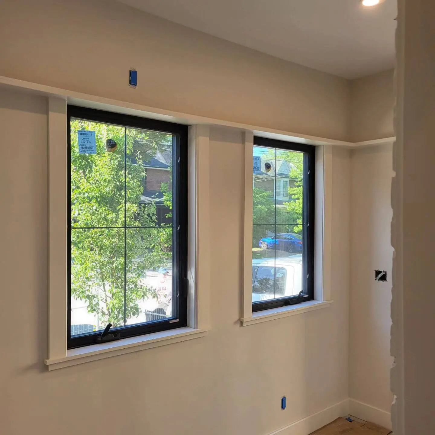 Two large windows framed in white, overlooking a tree-lined street. Two large windows framed in white, overlooking a tree-lined street.