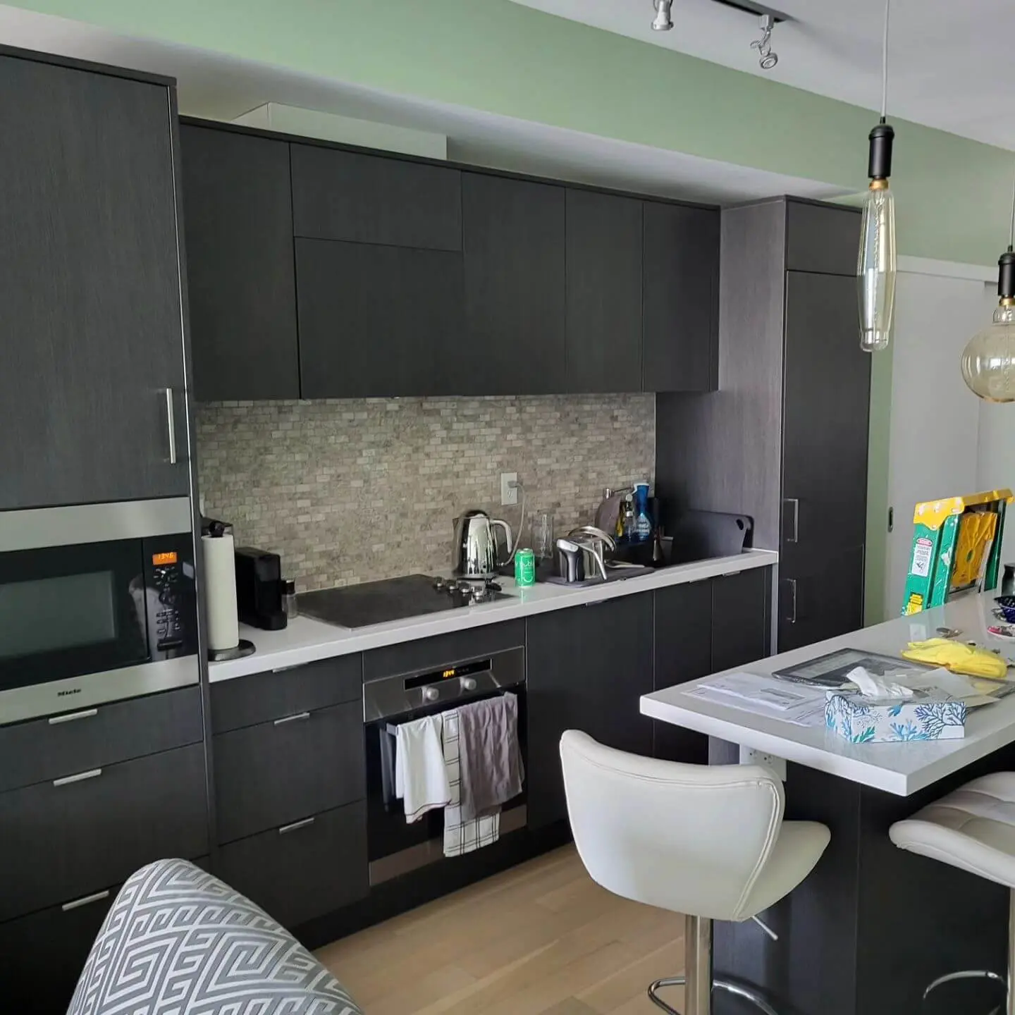 Modern kitchen with dark cabinets, a white countertop, and tiled backsplash, featuring appliances like a microwave, oven, and sink.