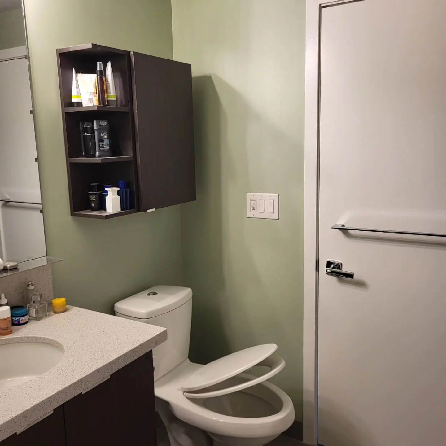 Bathroom with a green wall, dark floating cabinet, white countertop, toilet, and a closed door with a towel bar.