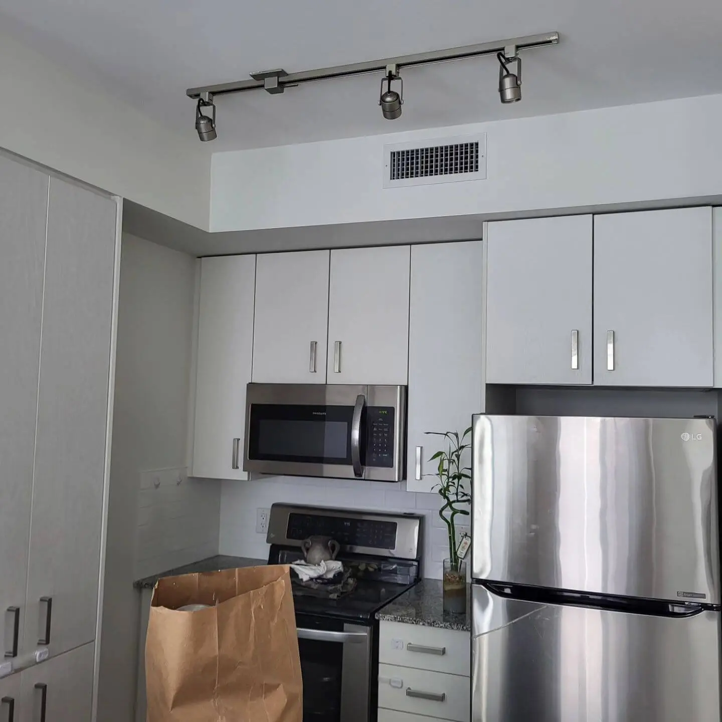 Compact kitchen area with white cabinets, stainless steel appliances including a refrigerator, microwave, and oven, and a granite countertop. Compact kitchen area with white cabinets, stainless steel appliances including a refrigerator, microwave, and oven, and a granite countertop.