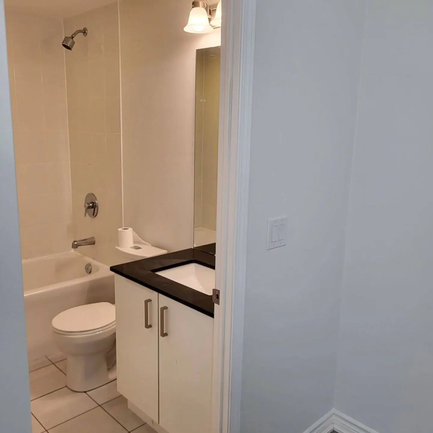 Bathroom with a bathtub, black vanity, and large mirror illuminated by a sconce light.