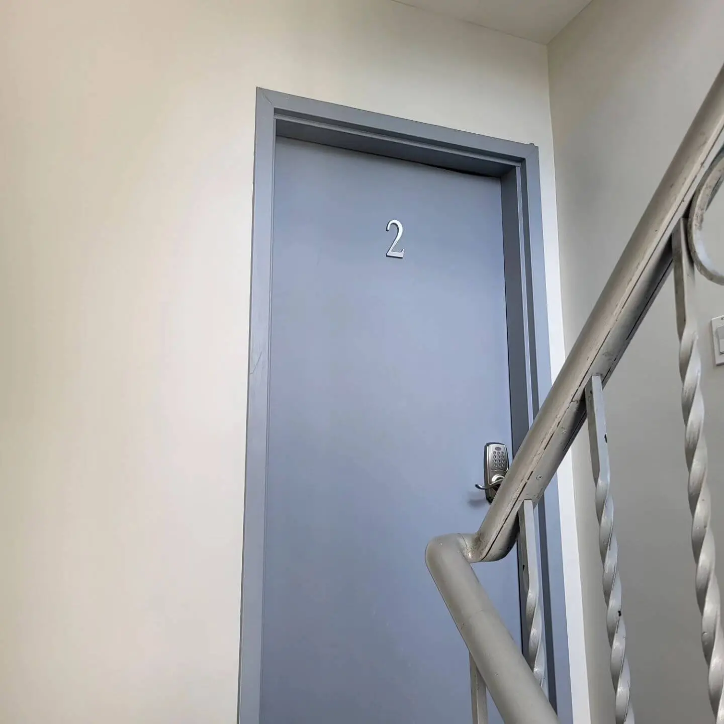 A door labeled '2' on the second floor landing with a metal railing in the foreground.