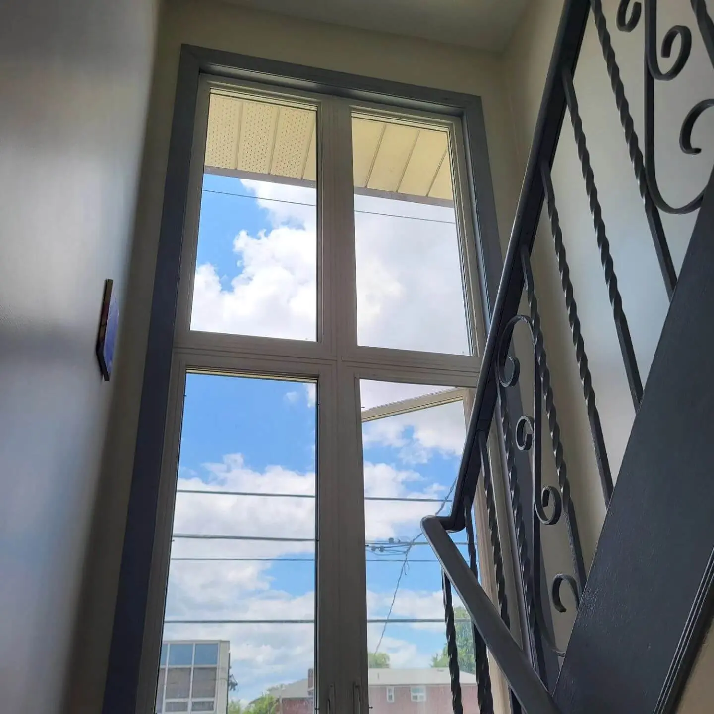 Tall window with black metal railing and a view of the sky with clouds.