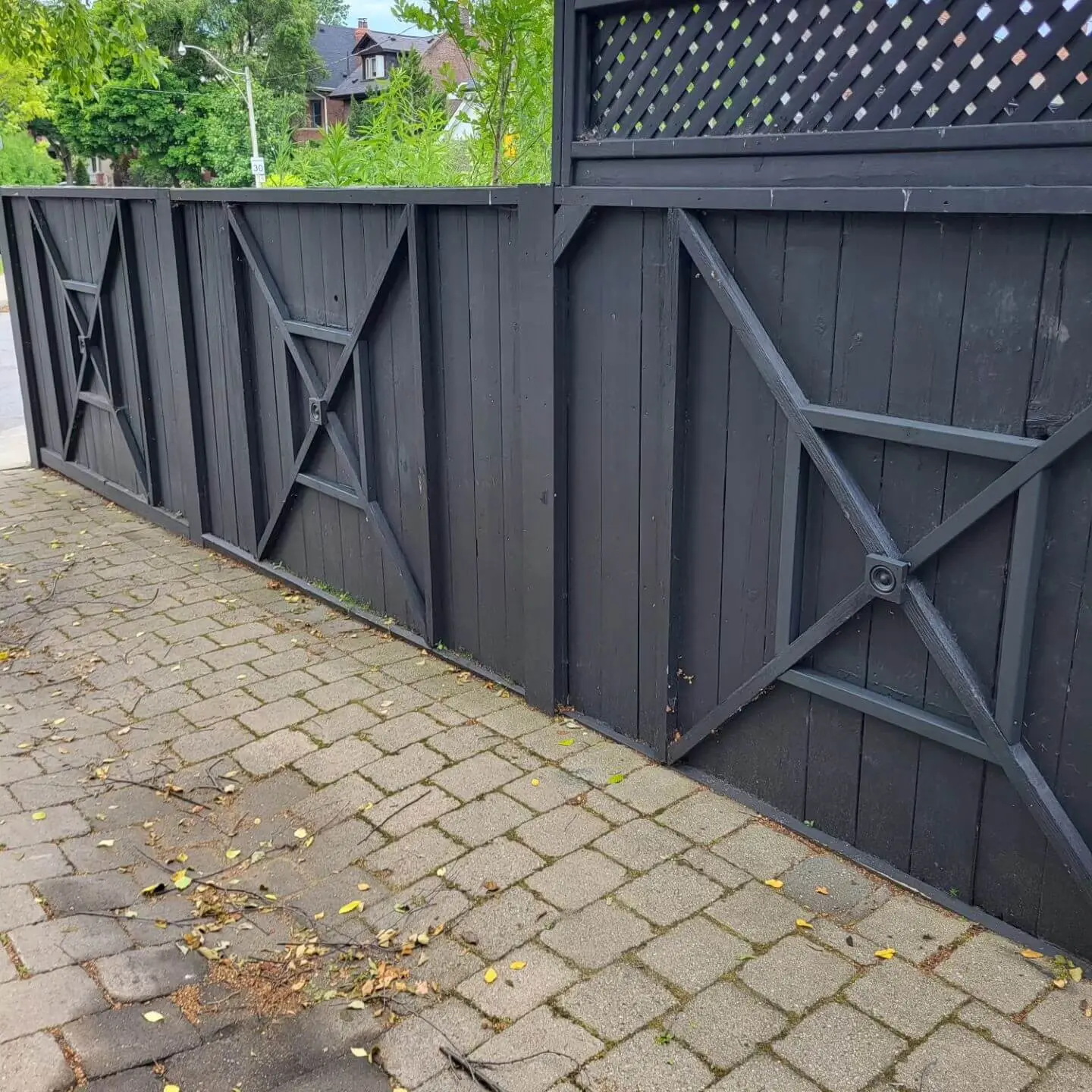 Black wooden fence with an X-pattern design, alongside a brick walkway.
